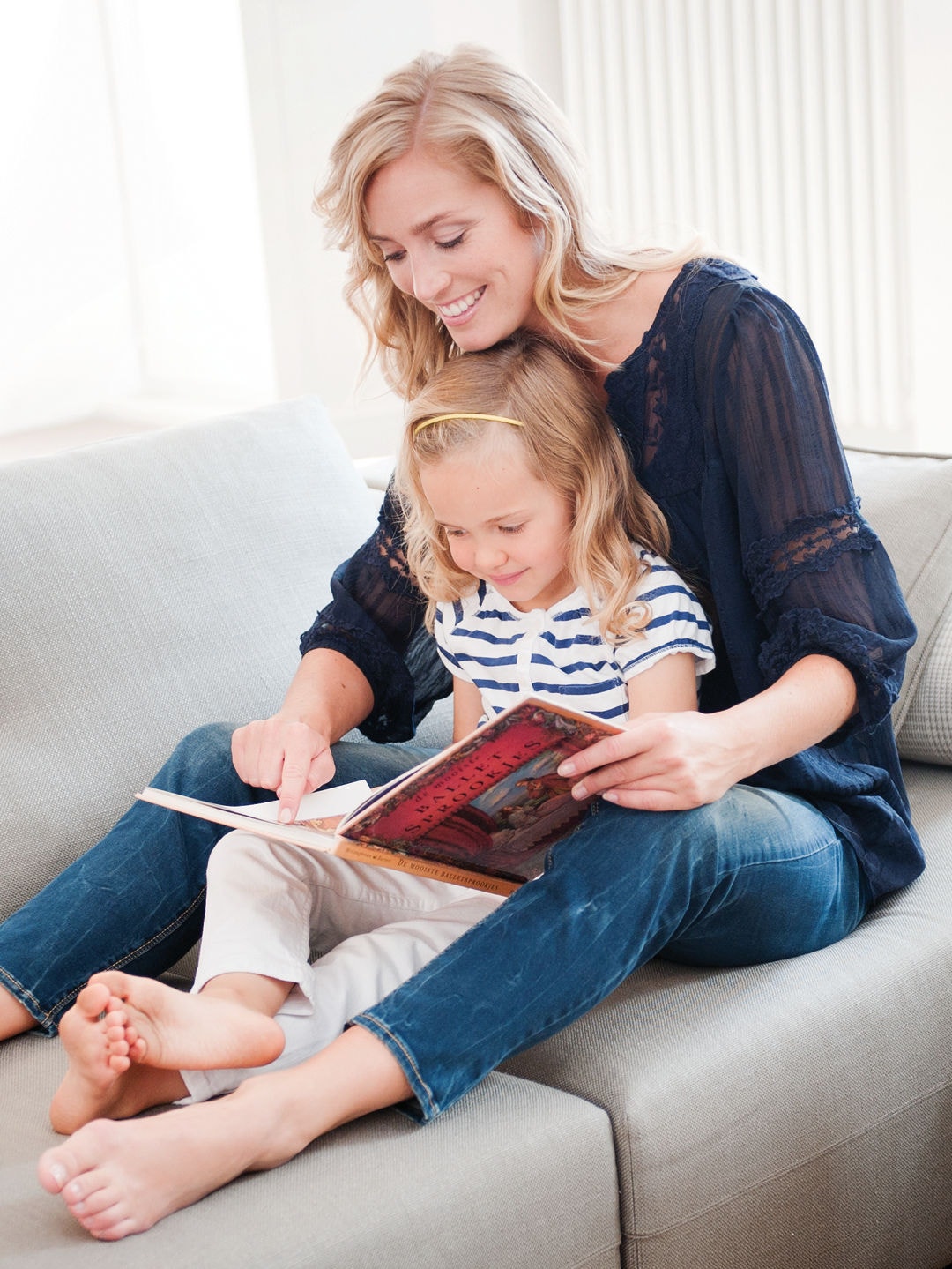 Mom and little daughter sitting on her lap looking at book on the couch