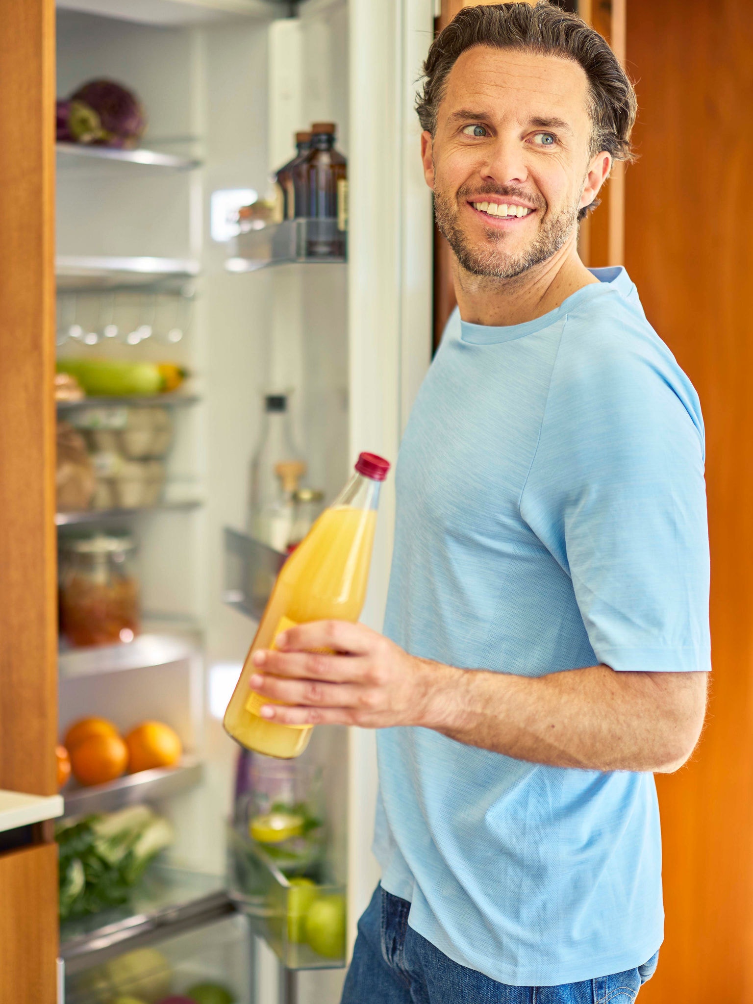 Man opening a refrigerator and taking out a bottle of orange juice