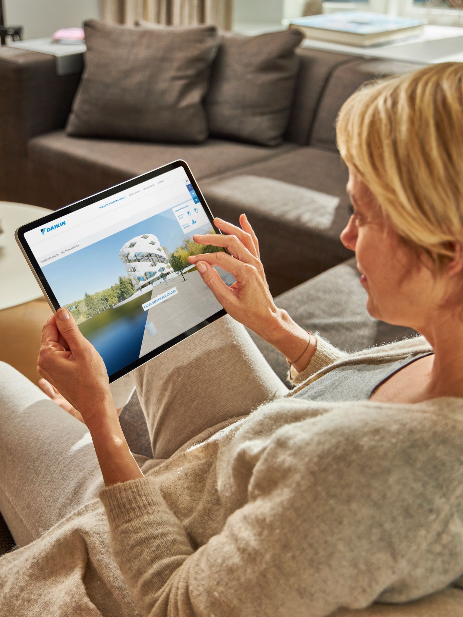Woman sitting on a sofa viewing air conditioners on the virtual experience centre on his tablet
