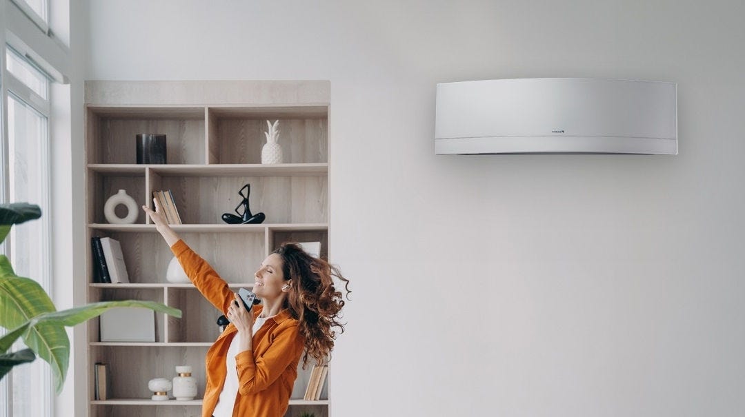 Discreet wall-mounted heat pump in a room with sage green walls above a decorative shelf