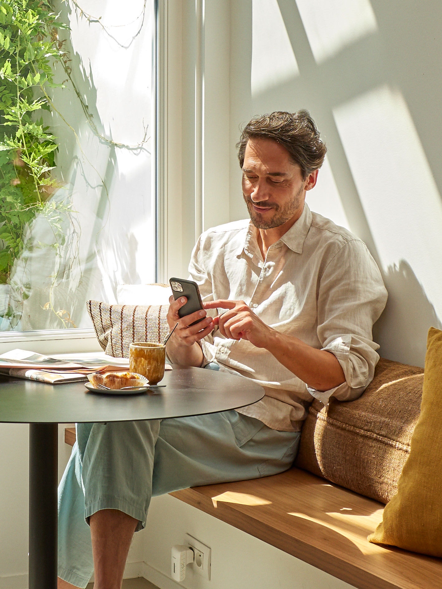 Man relaxing and looking at his phone sat at a table with a cup of coffee and some food in front of him