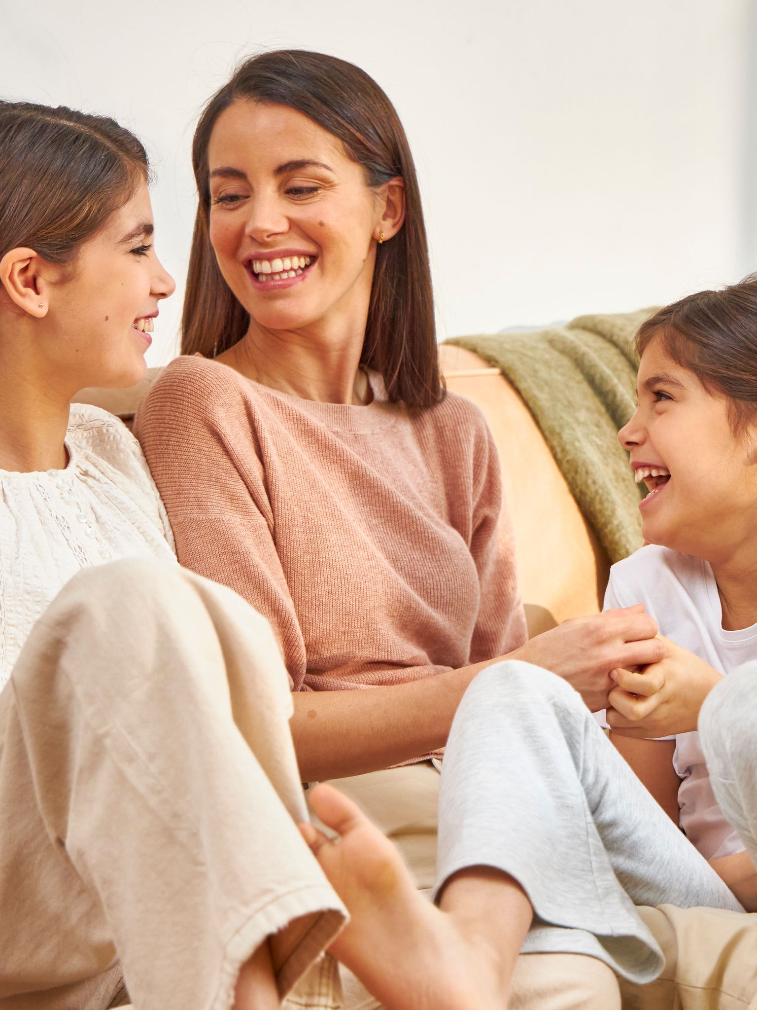 Mother and two daughters laughing while sitting on the couch