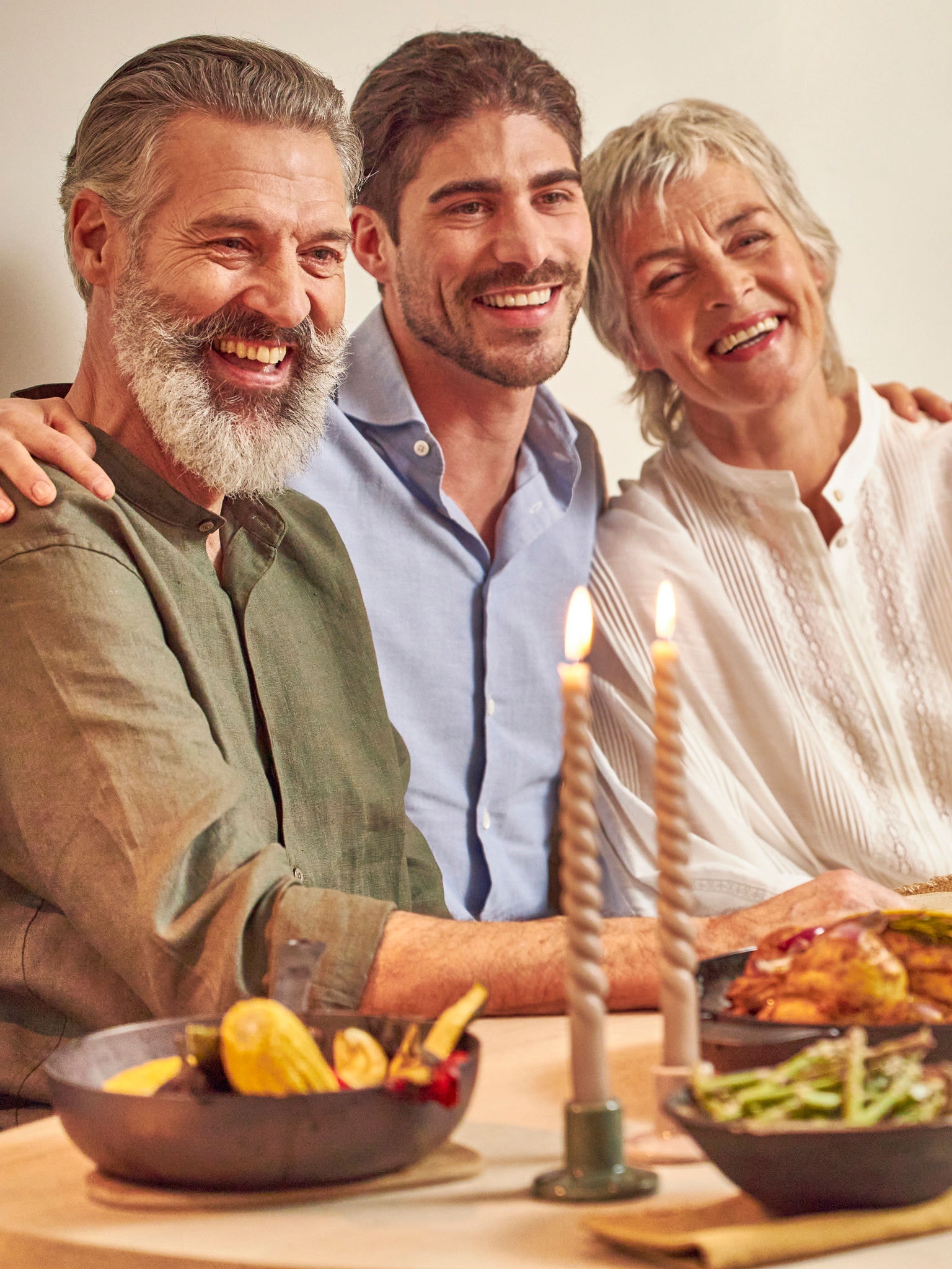 Adult son with his parents happily sitting at the dinner table